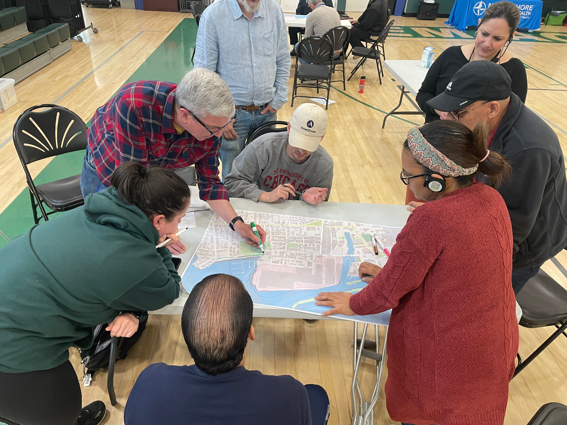 Close-up of a multi-generational group around a printed neighborhood map, marking locations and discussing priorities.